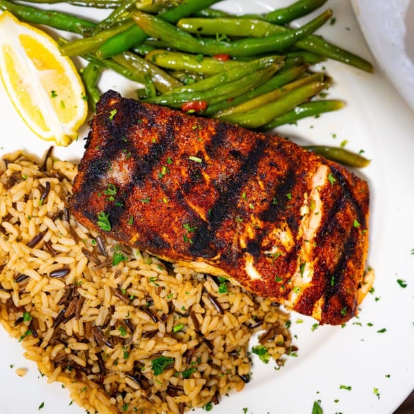 Blackened fish with rice pilaf, green beans, and a lemon wedge on a white plate.