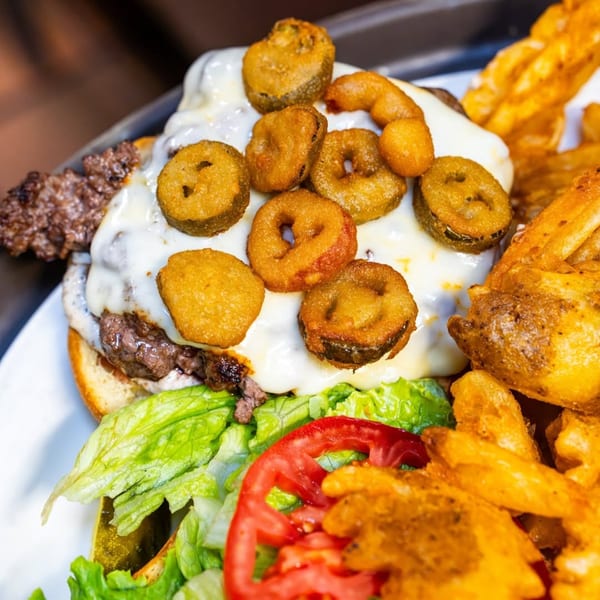 P&G’s American burger with melted cheese, fried pickles, lettuce, tomato, and a side of fries.