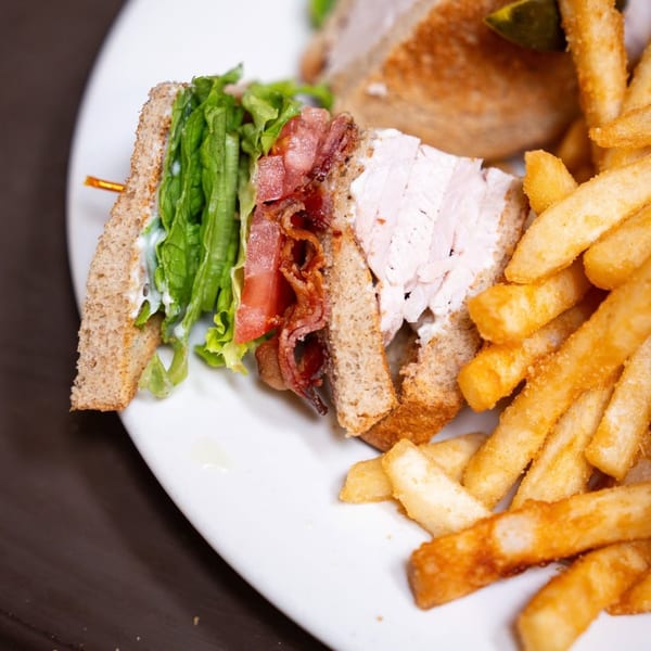 A P&G's club sandwich with turkey, bacon, lettuce, and tomato, served with golden fries.