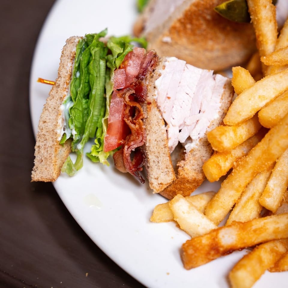 A P&G's club sandwich with turkey, bacon, lettuce, and tomato, served with golden fries.
