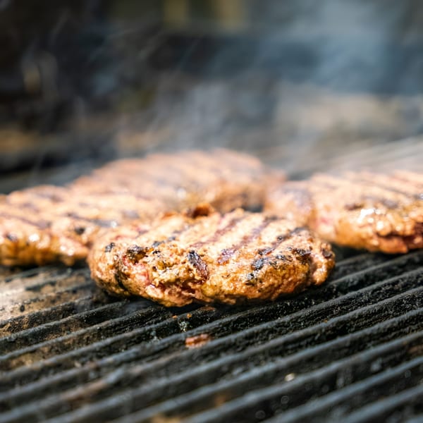 P&G's American burgers sizzling on a hot grill with smoke rising.