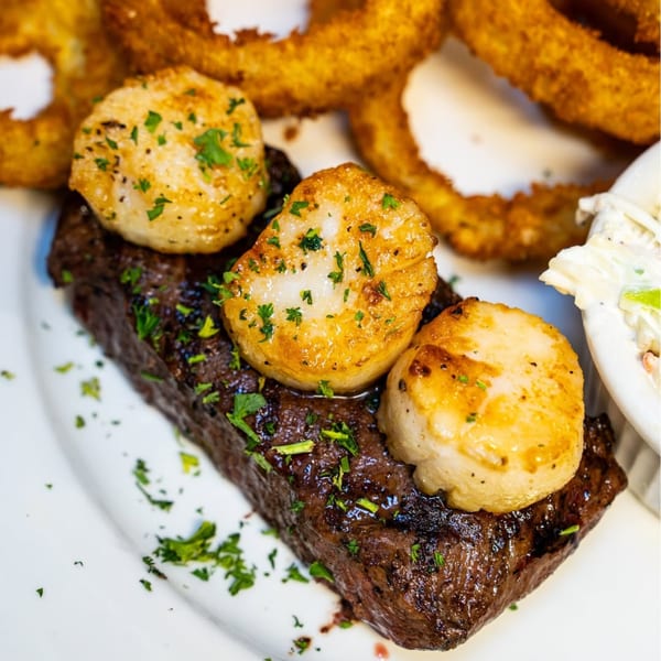 P&G's surf and turf with steak, scallops, onion rings, and coleslaw on a white plate.